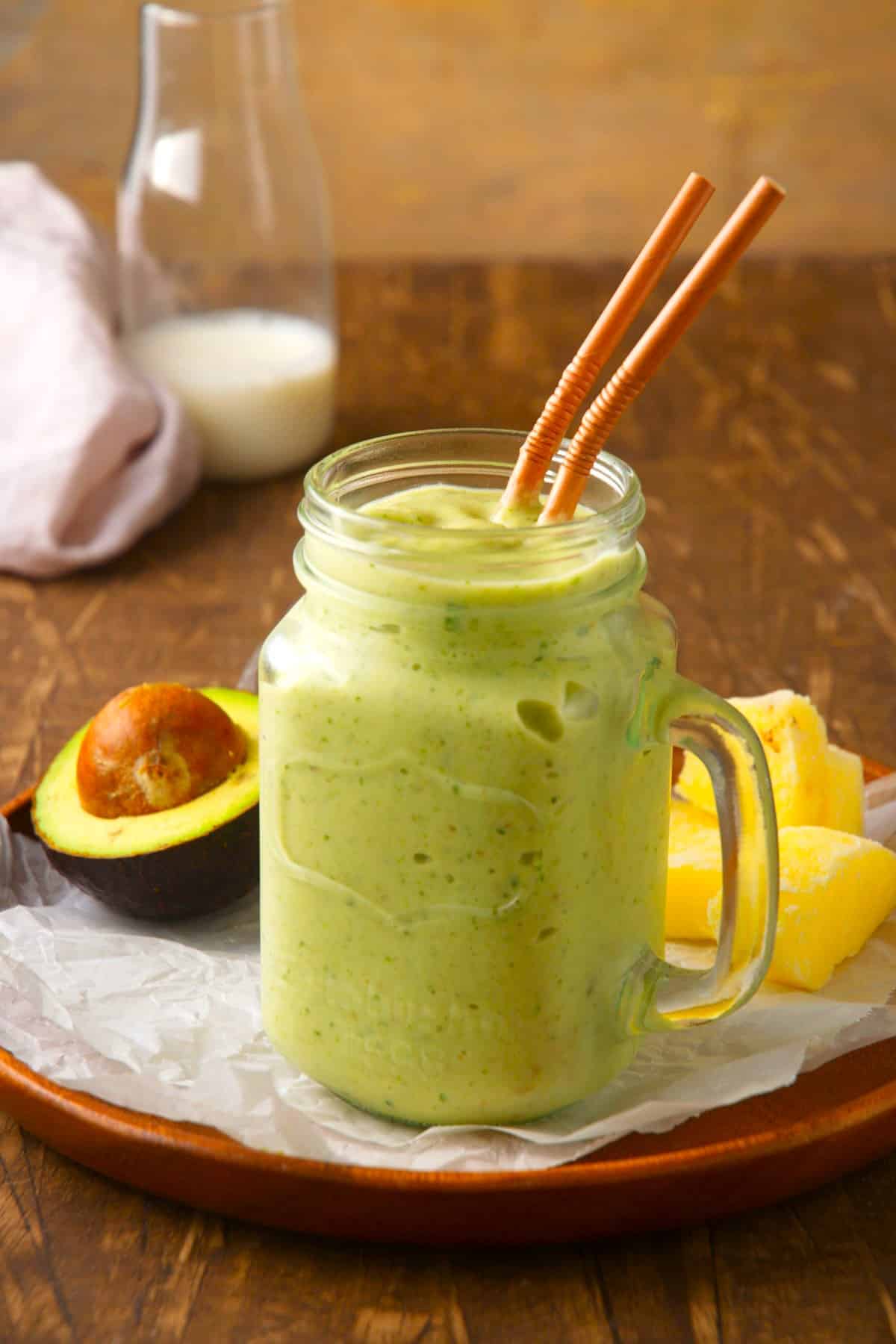 Avocado smoothie with two brown straws in glass jar.