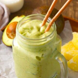 Avocado smoothie with two brown straws in glass jar.