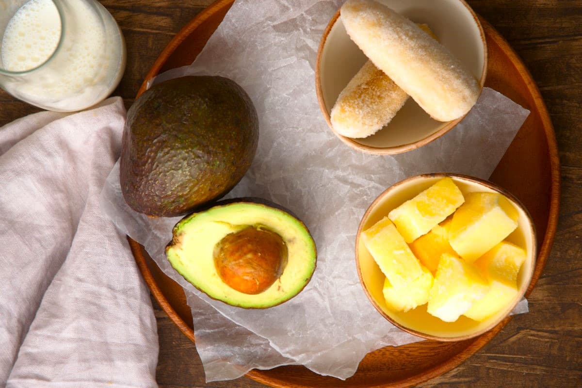 Avocado smoothie ingredients prepped on wooden background.