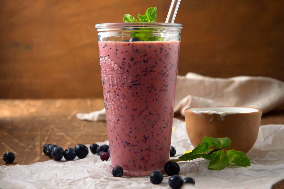 Blueberry smoothie in glass with fresh mint, blueberries and a clear straw.