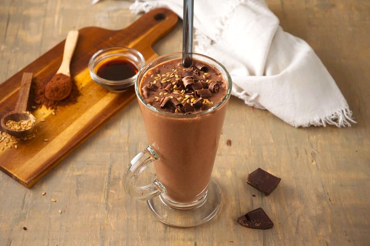 Chocolate banana smoothie in glass topped with chocolate curls and flax seeds.