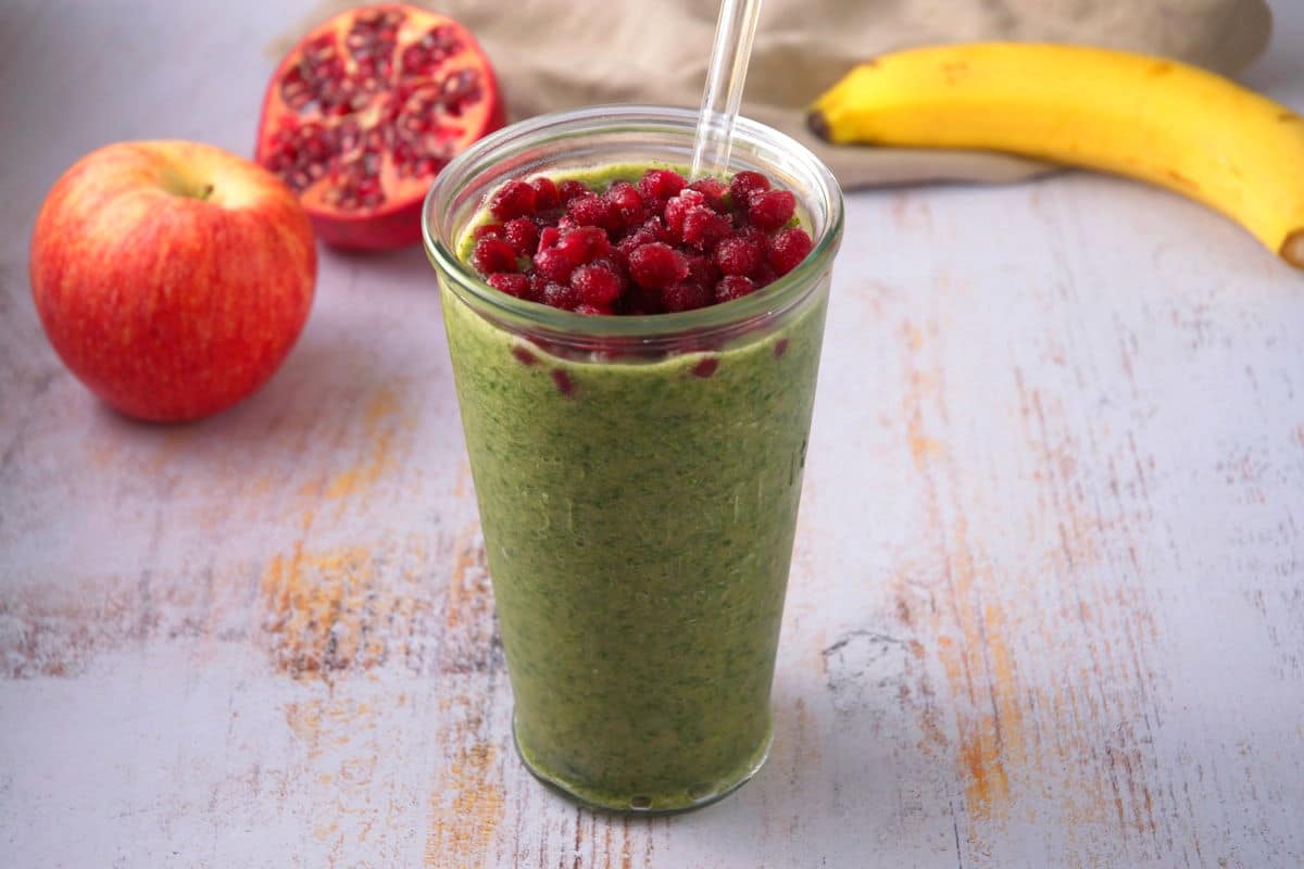 Kale smoothie with pomegranate seed topping in glass.