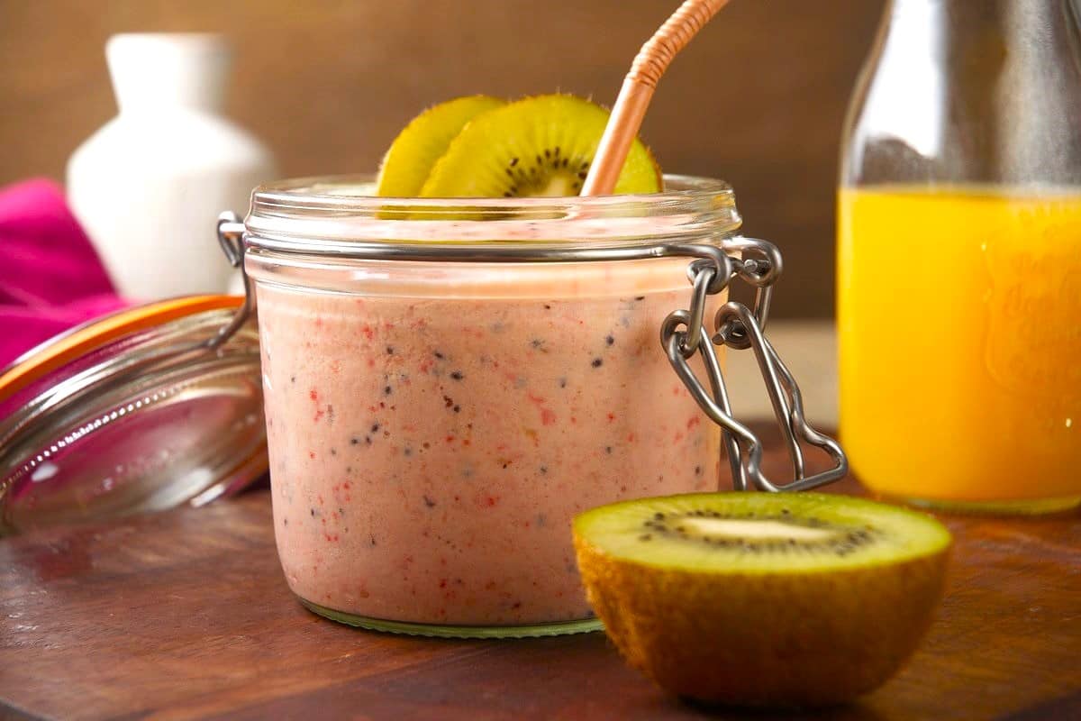 Kiwi smoothie in jar with brown straw and kiwi slices.