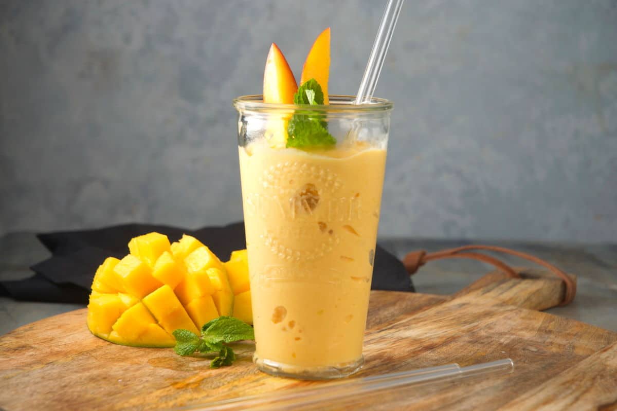 Mango smoothie with mint in a glass and fresh mango on the side.