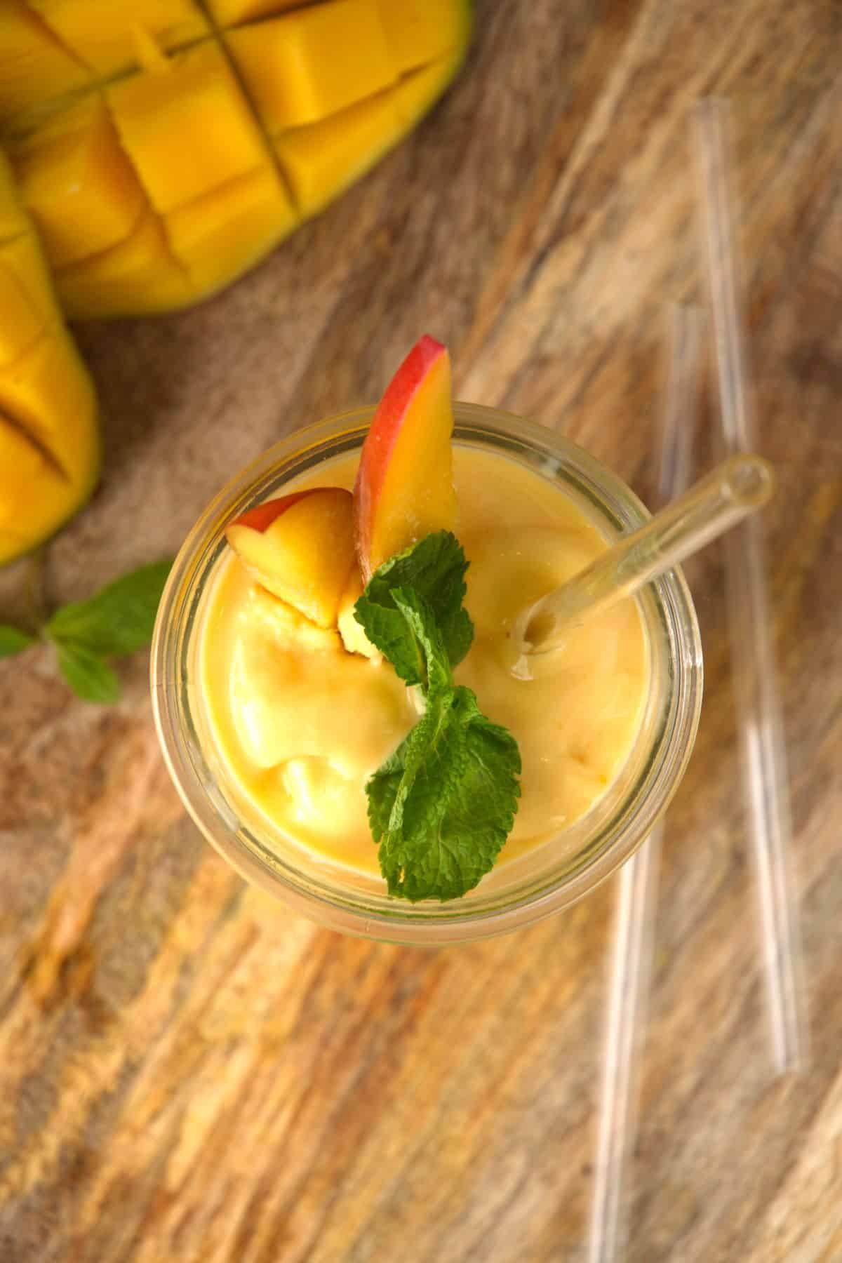 Top view of mango smoothie with mint and clear straw.