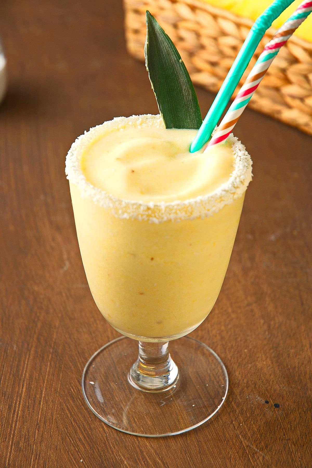 Piña Colada smoothie in glass with straws and coconut rim.