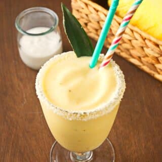 Piña Colada smoothie in glass with pineapple leaf and straws.