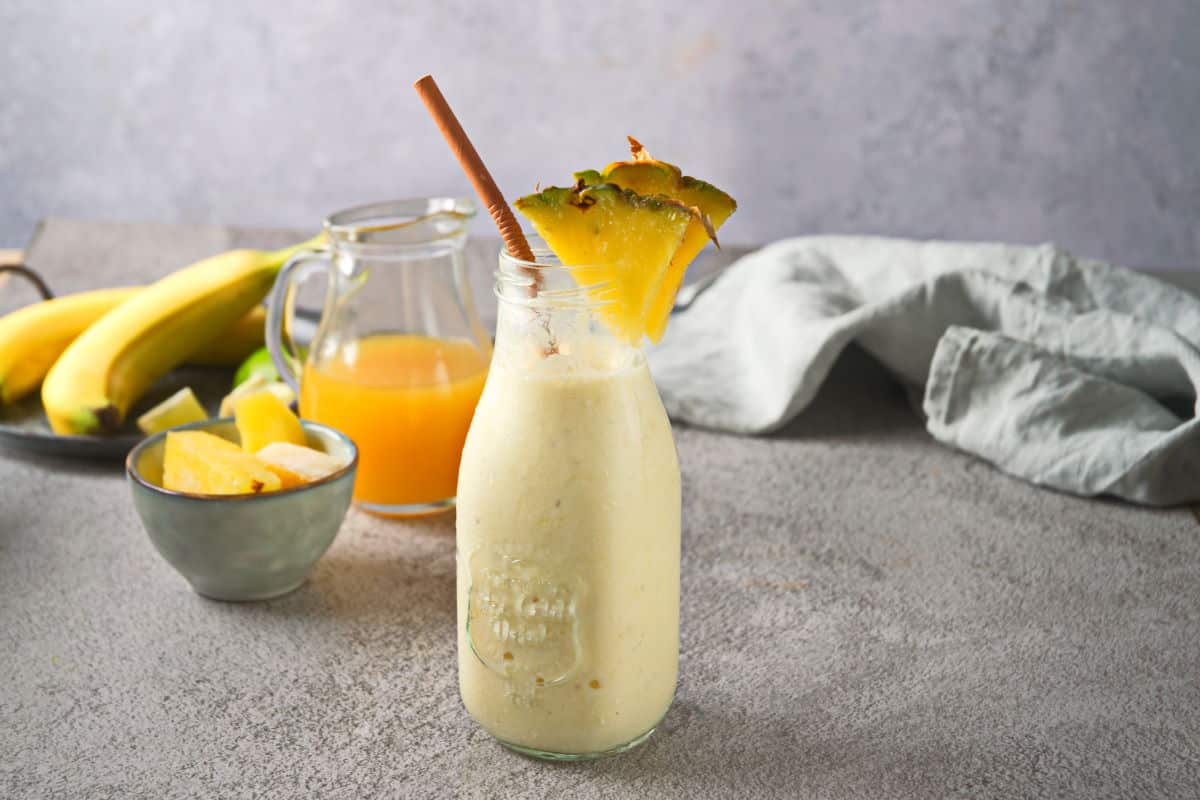 Pineapple smoothie in a jar with pineapple wedges and straw.