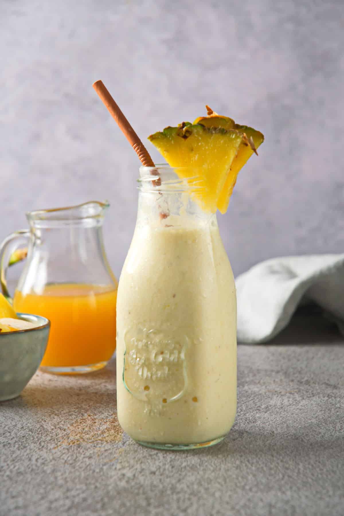 Pineapple smoothie in a jar with pineapple wedge and straw.