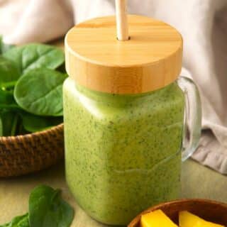 Spinach smoothie in glass jar with wooden lid and straw.