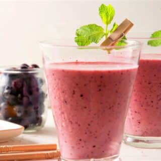 2 glasses with strawberry-blueberry smoothie and fresh mint garnish.