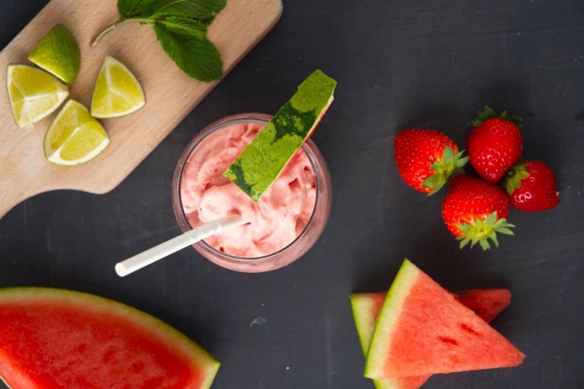 Watermelon smoothie with fresh watermelon wedges and paper straw in glass.