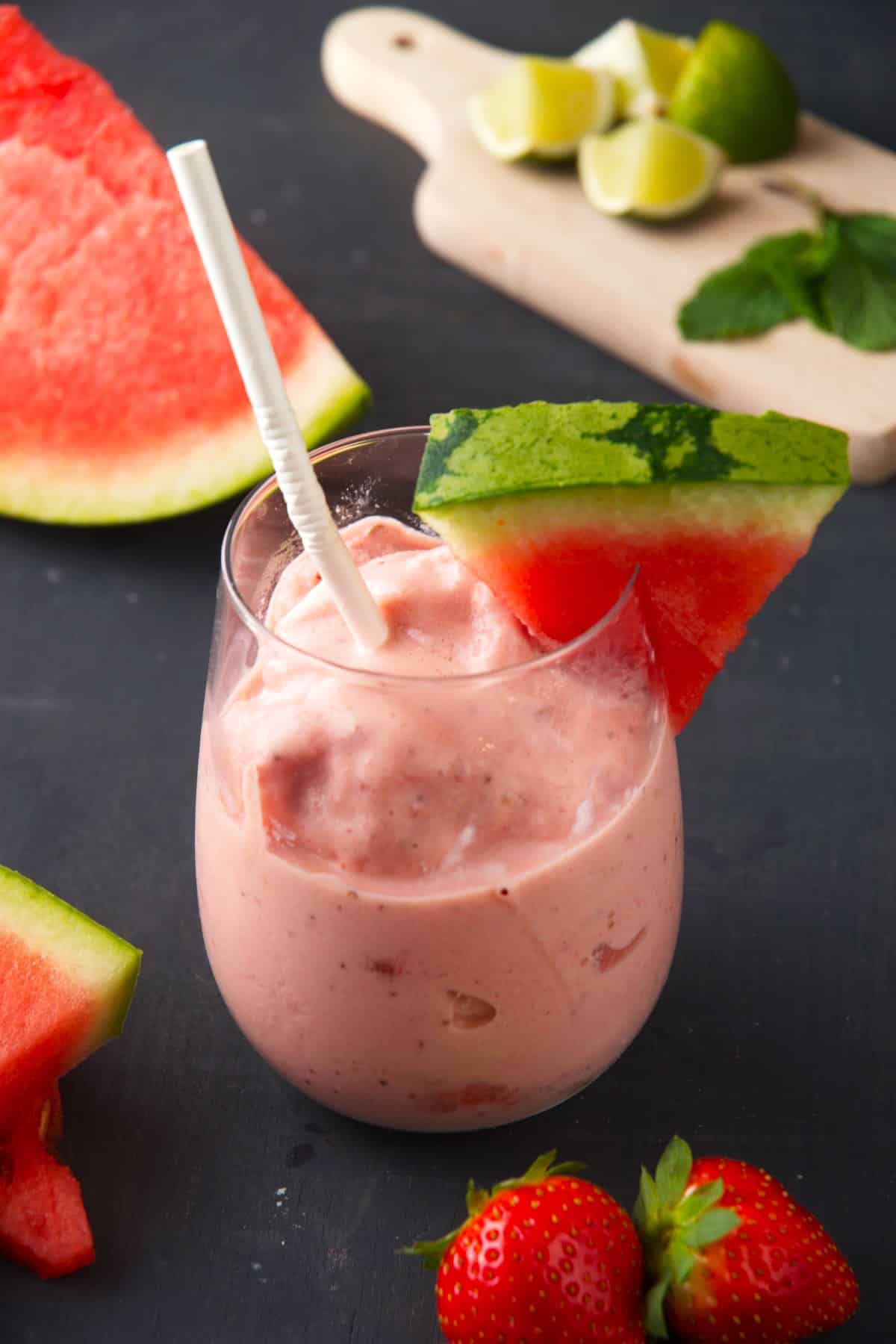 Watermelon smoothie with fresh watermelon wedge and paper straw in glass.