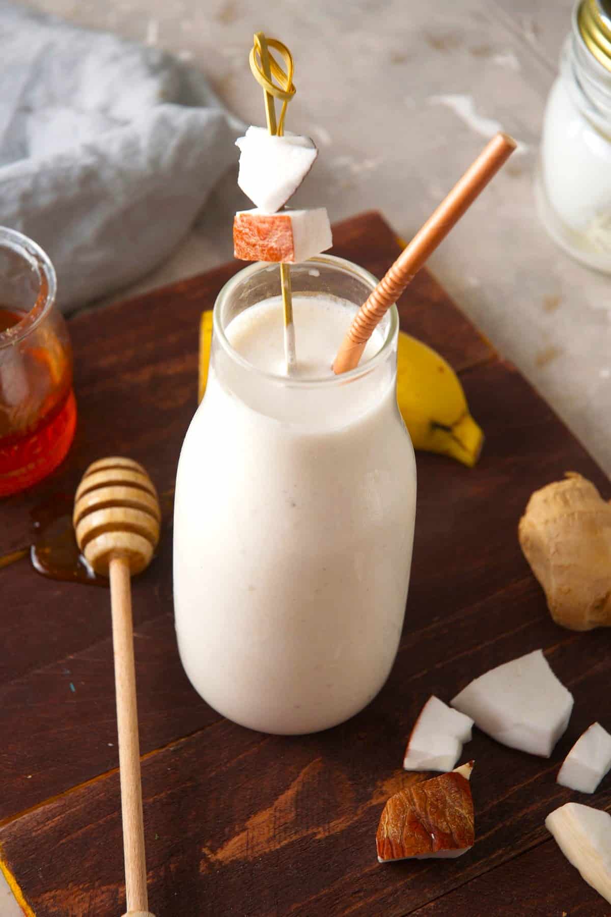 Greek yogurt smoothie in glass with straw and chunks of coconut as a garnish.