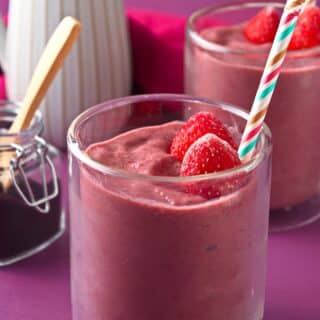 Acai smoothie in glass with frozen strawberries.