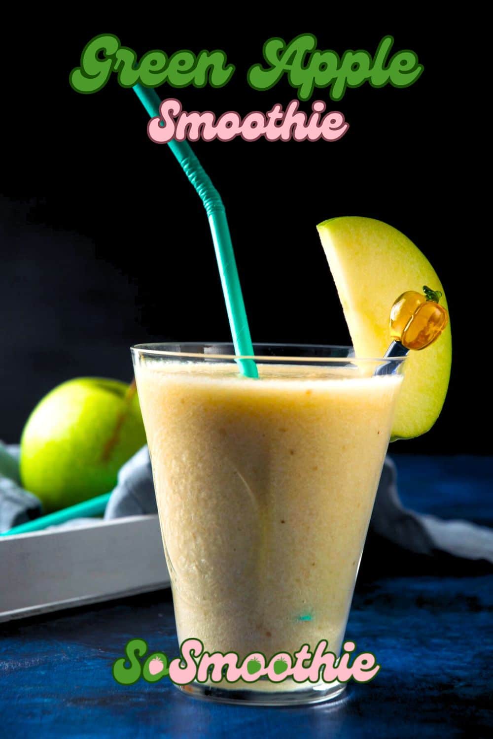 Green apple smoothie in glass with blue straw and apple slice, black background.