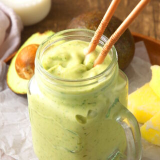 Avocado smoothie in jar with two straws.