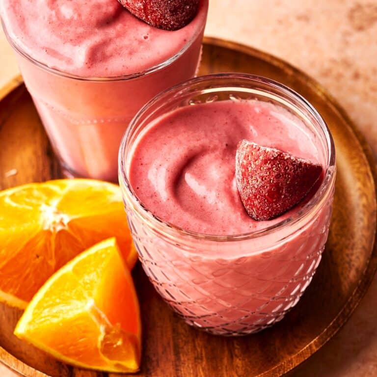 Beet smoothie in glasses with frozen strawberry garnish.