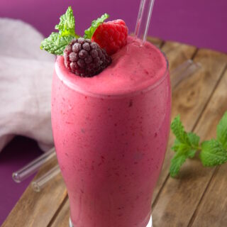 Triple berry smoothie in glass with clear straw.