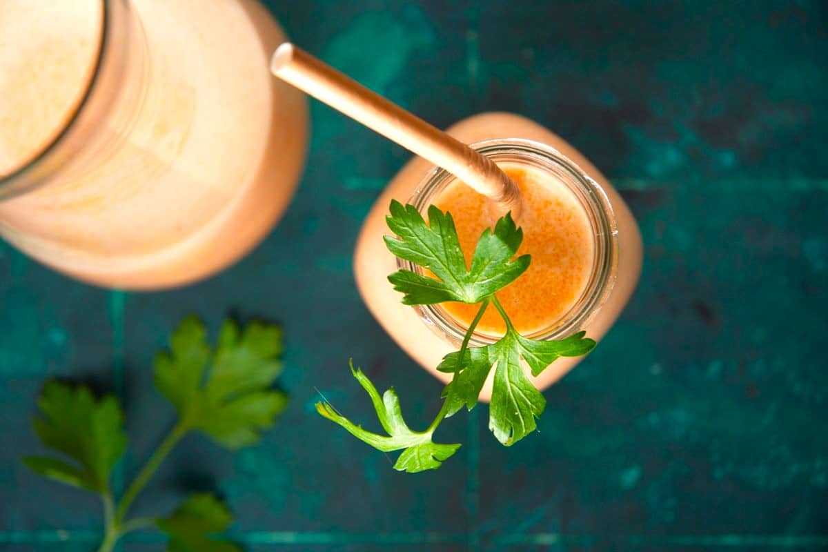 Carrot smoothie in glass with fresh parsley.