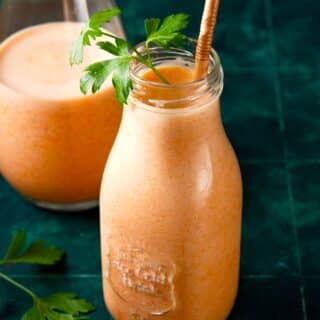 Carrot smoothie in glass with parsley and straw.