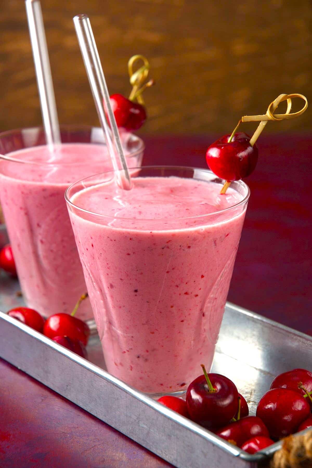 Cherry smoothies on metal serving dish with clear straws.