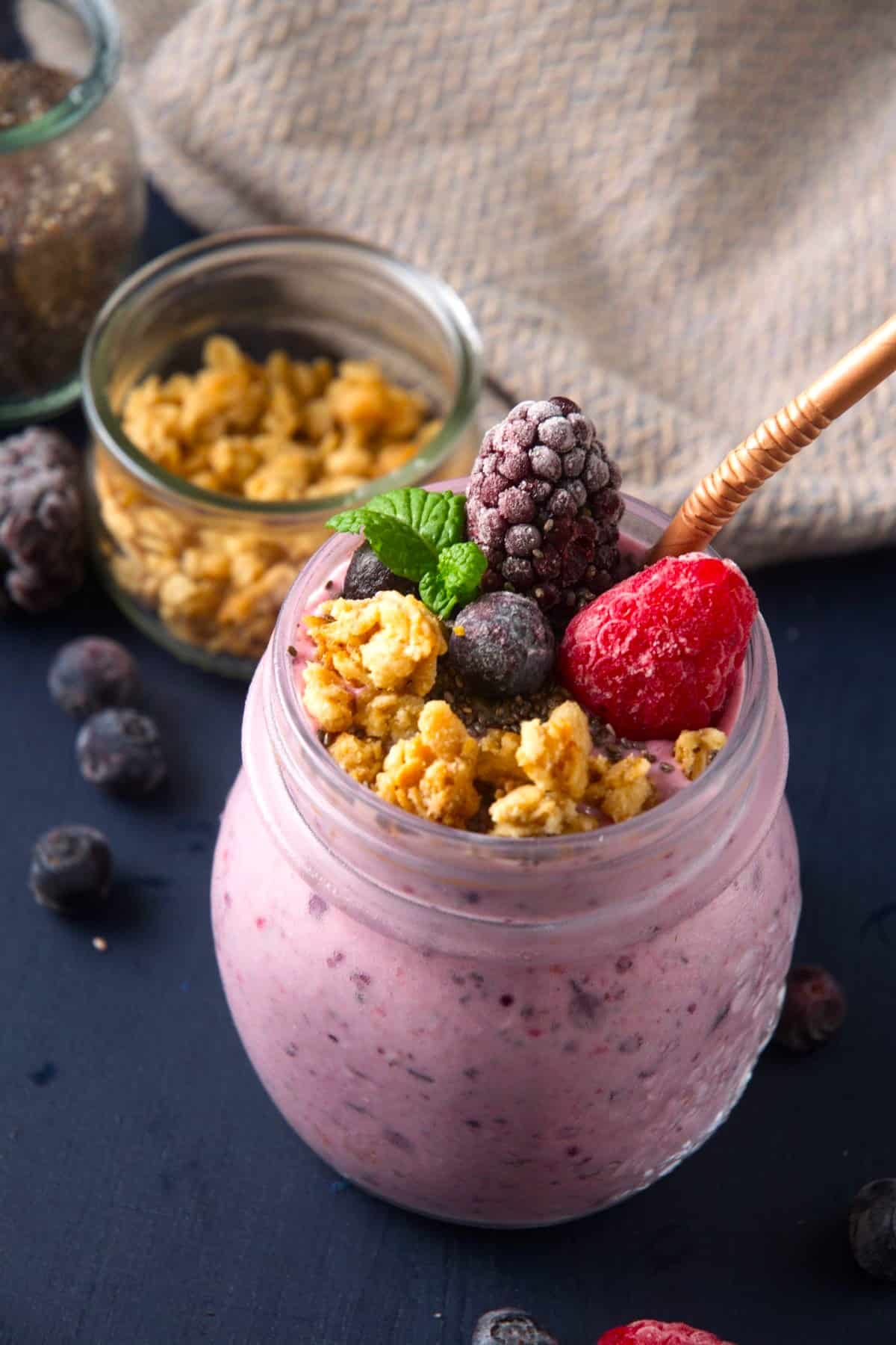 Chia seed smoothie in jar with straw, topped with granola and mixed berries.