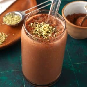 Chocolate peanut butter smoothie in glass with straw and topped with hemp seeds and cocoa powder.