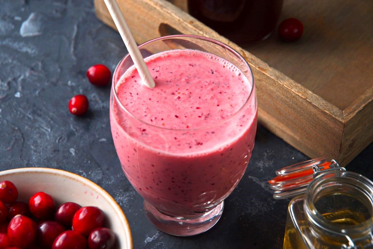 Cranberry smoothie in glass on blue background.