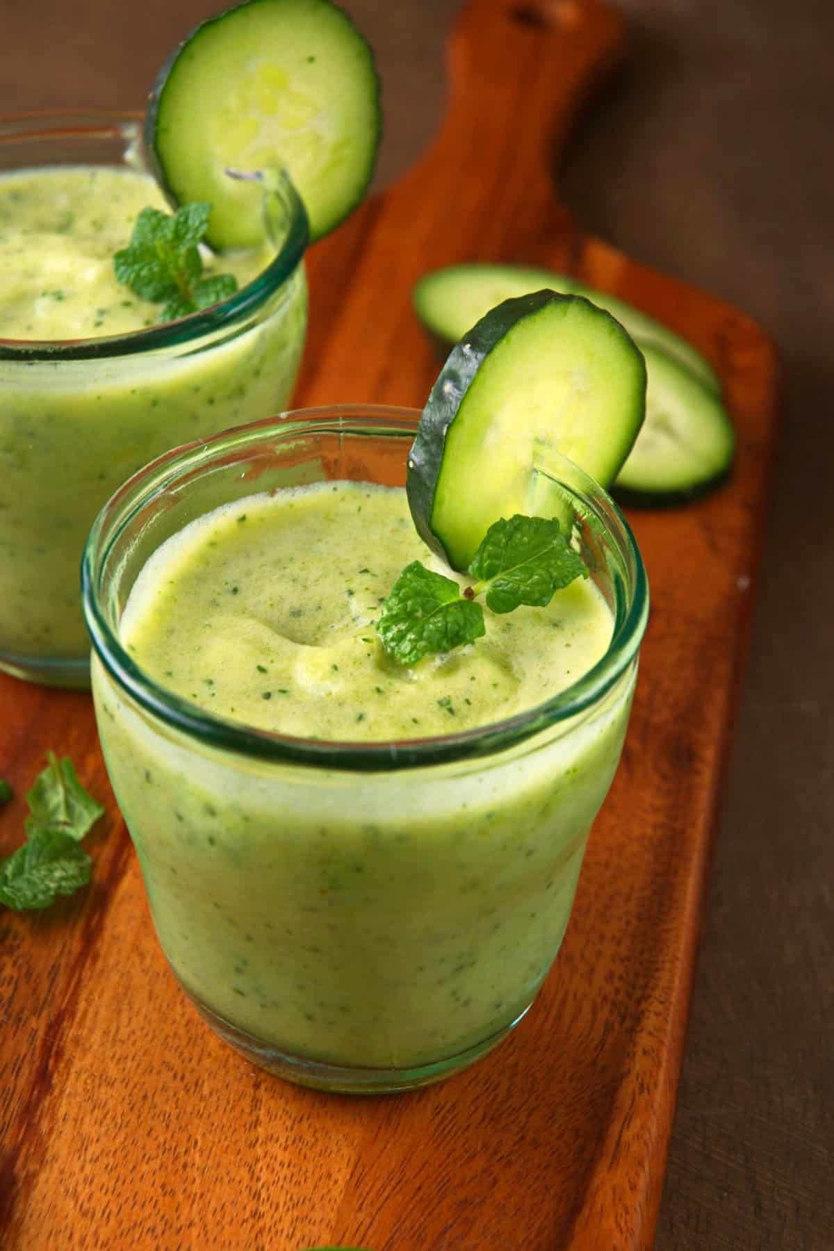 Cucumber smoothie in glasses on wooden board.
