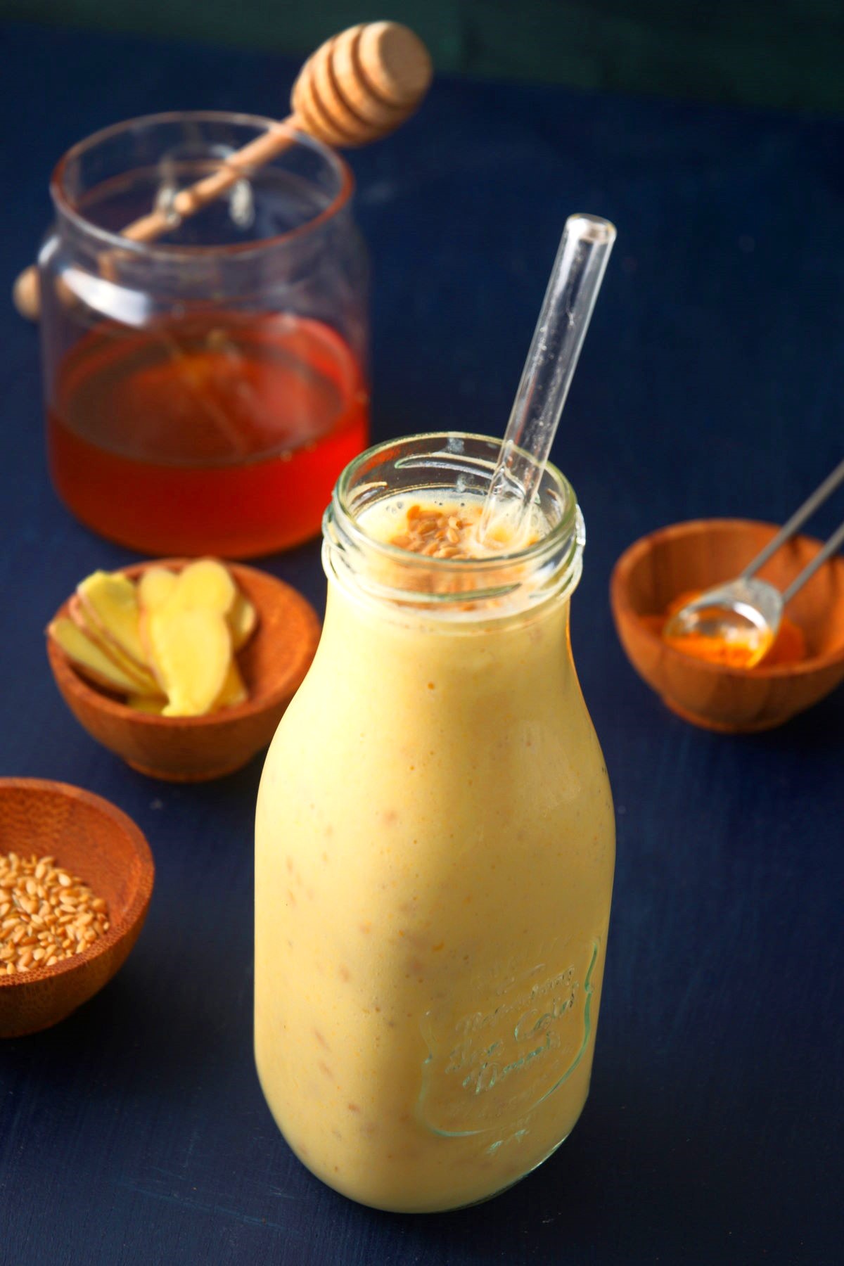 Flax seed smoothie in glass jar with straw and honey on the side.