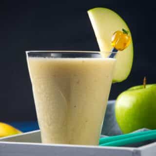 Green apple smoothie in glass with apple slice.