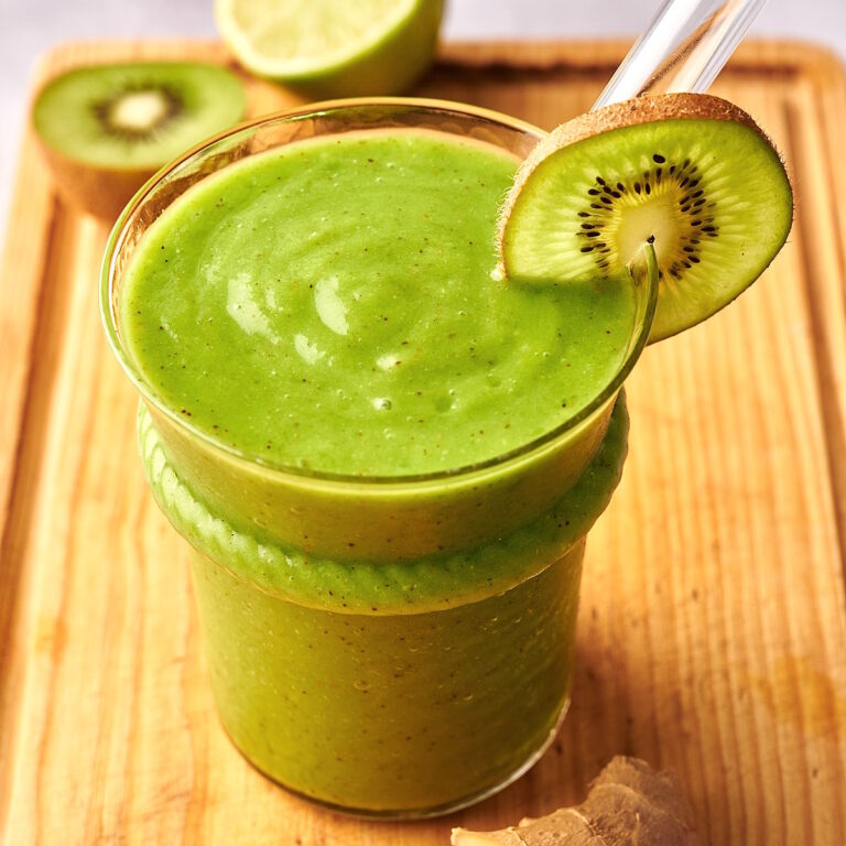 Green smoothie on cutting board with clear straw and kiwi slice.