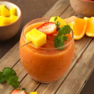 Mango strawberry smoothie in glass with fruit skewer and mint.
