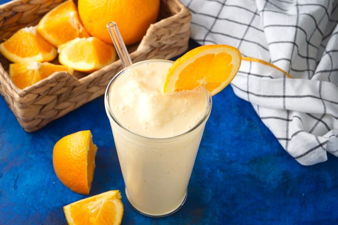 Orange smoothie in glass with orange slice and clear straw.