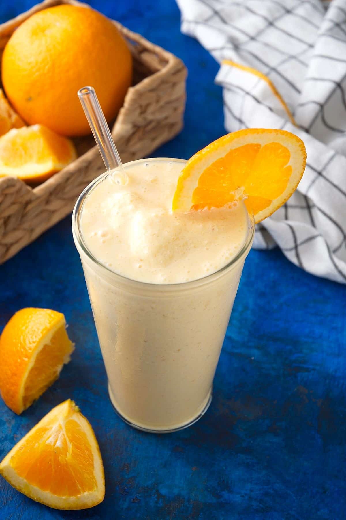 Orange smoothie in glass with orange slice on blue background.
