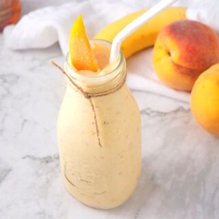 Peach smoothie in a glass with a peach slice garnish and straw.