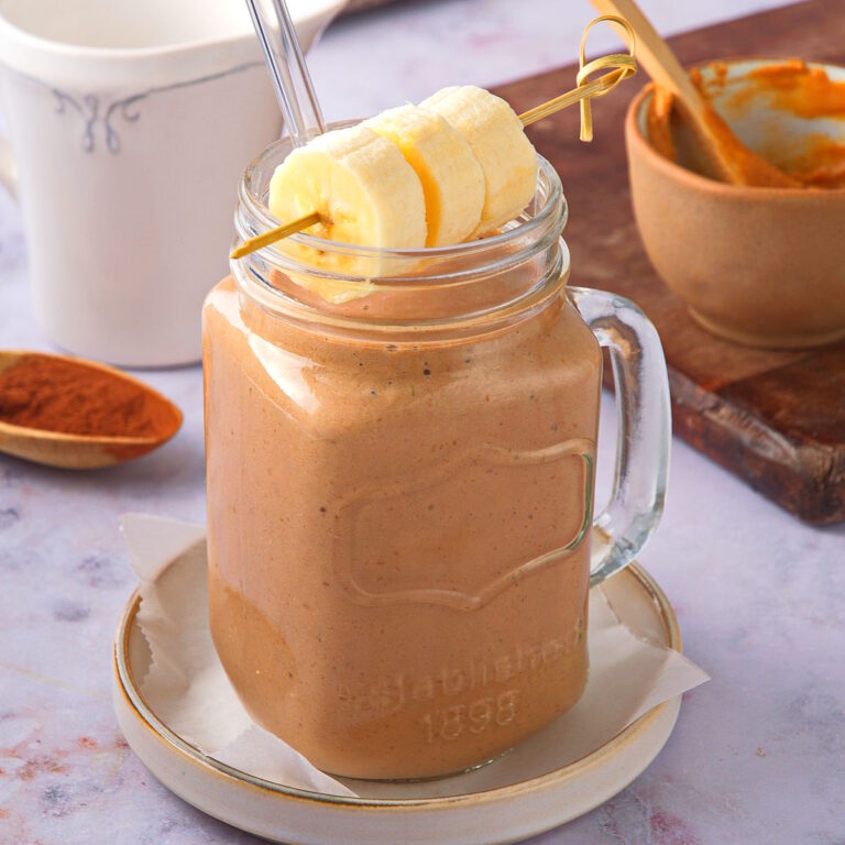 Peanut butter banana smoothie in glass with banana skewer.