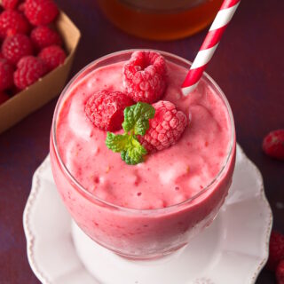 Raspberry smoothie in glass with red and white straw.