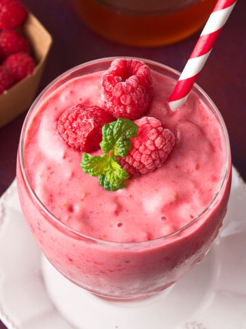 Raspberry smoothie in glass with red and white straw.