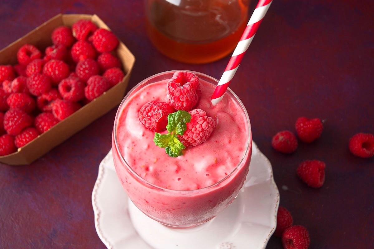 Raspberry smoothie in glass, surrounded by fresh raspberries.