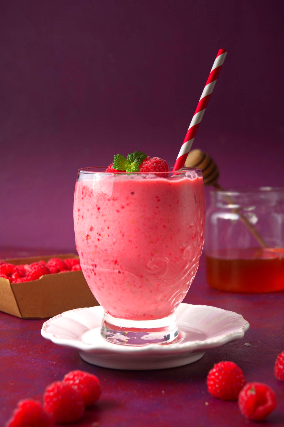 Raspberry smoothie in glass with purple background.