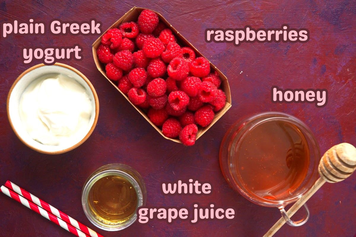 Raspberry smoothie ingredients prepped and labeled on purple-red background.