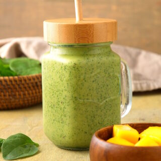 Spinach smoothie in glass jar with wooden lid and straw.