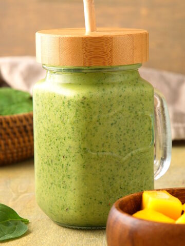 Spinach smoothie in glass jar with wooden lid and straw.