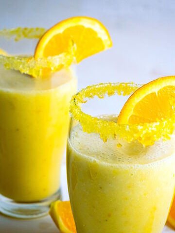 Vegan orange Julius in glasses with rim and orange slice.