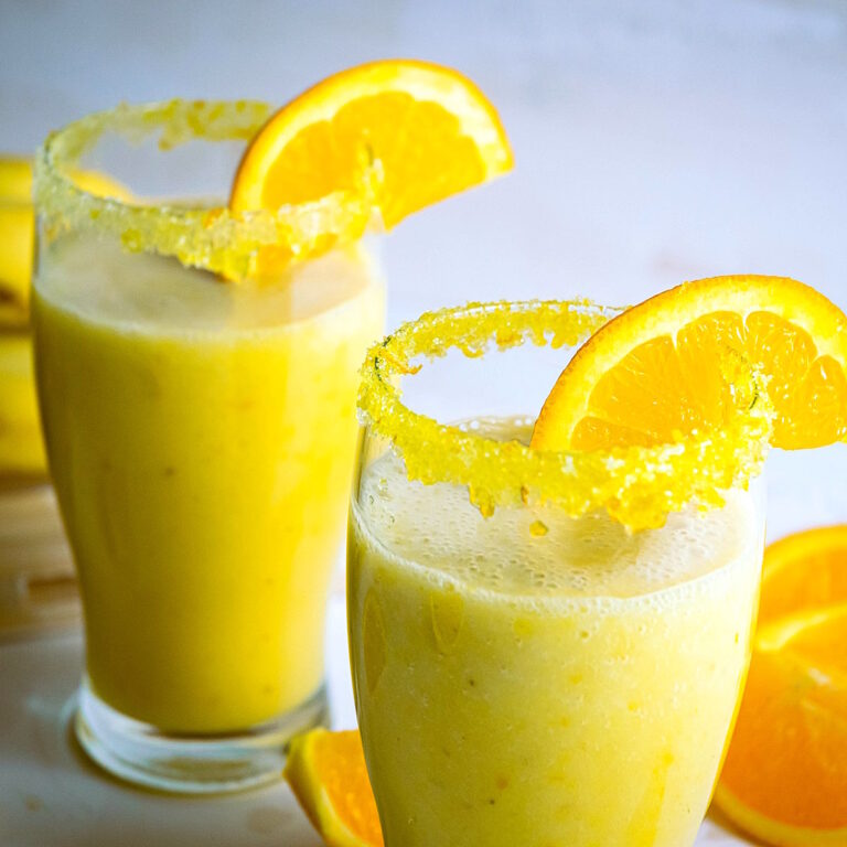 Vegan orange Julius in glasses with rim and orange slice.