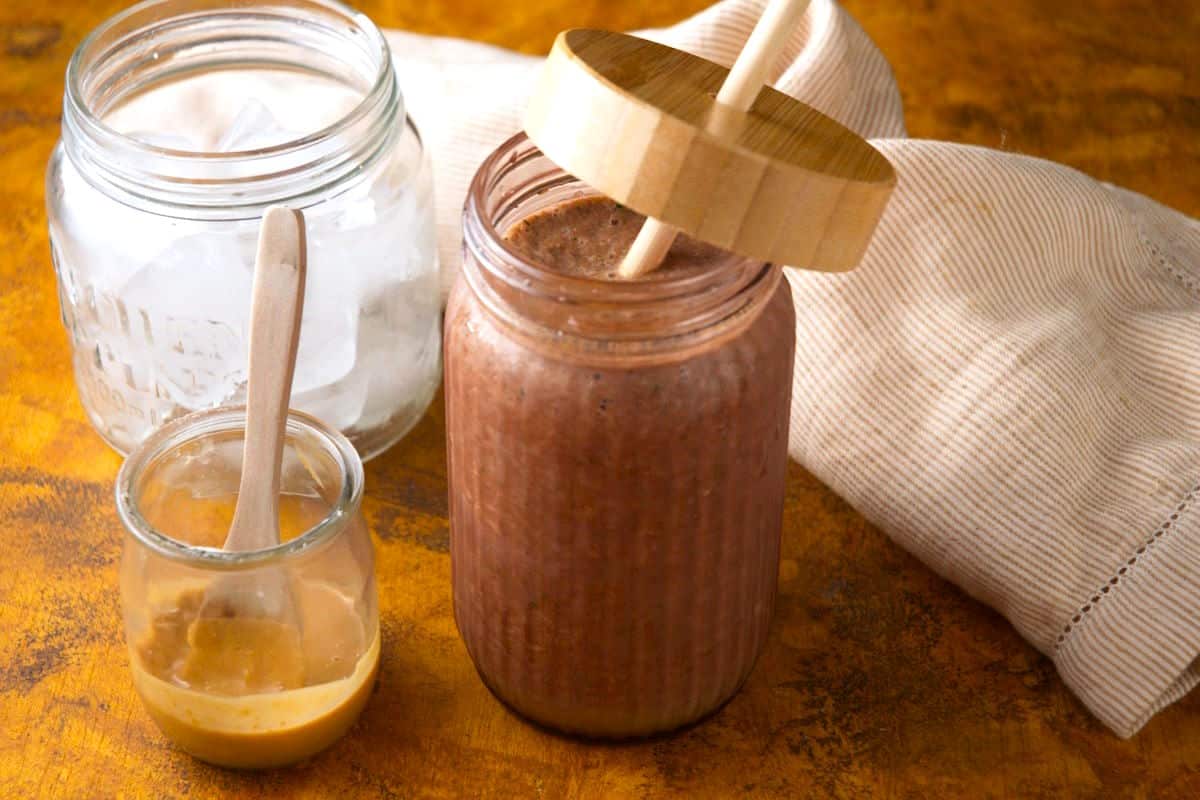 Chocolate zucchini smoothie in glass with wooden lid and straw.